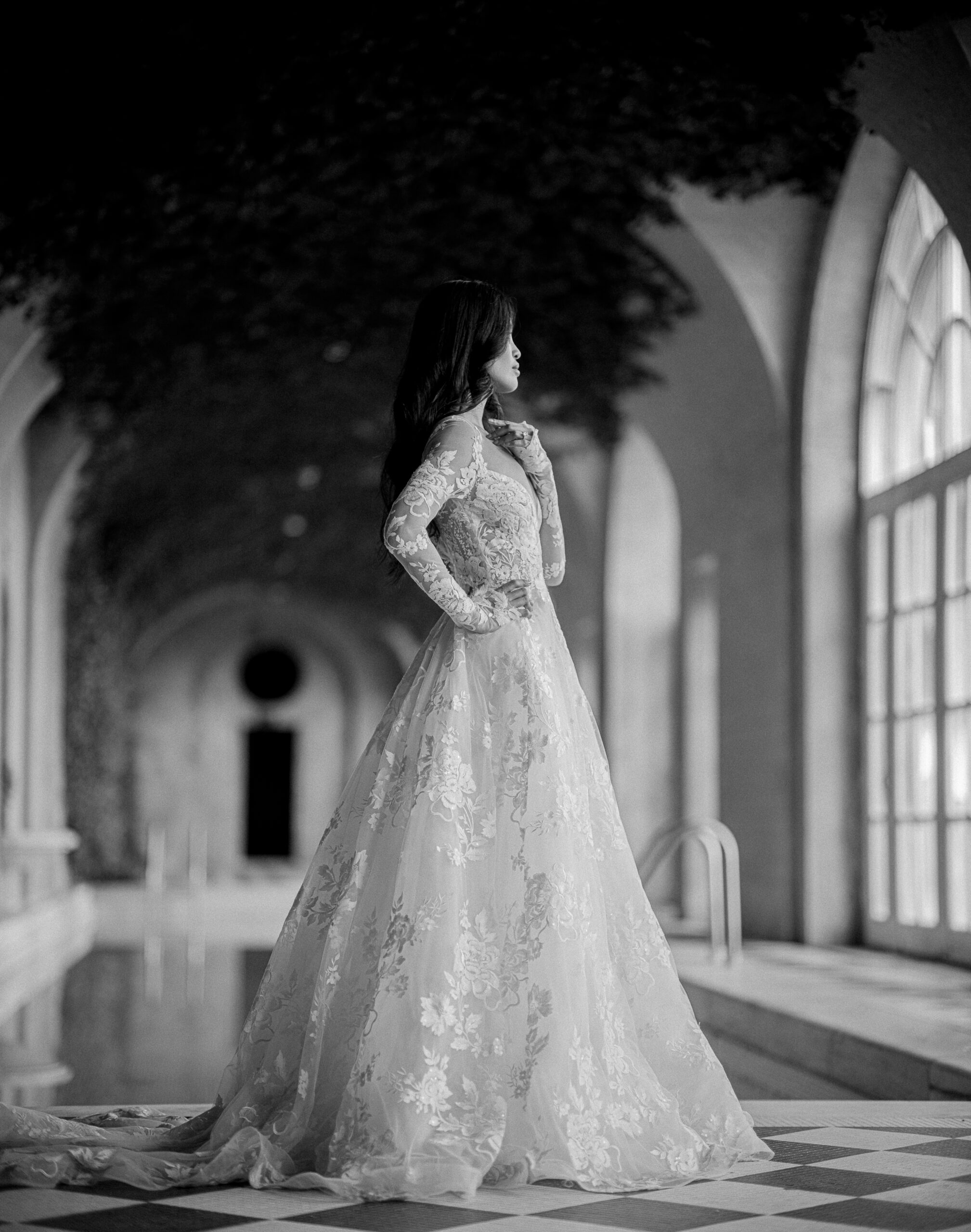 Bride in elegant gown by arched windows.